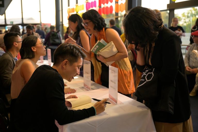 Author signing books for attendees at the OzAsia Festival Weekend of Words event inside a brightly lit venue space.